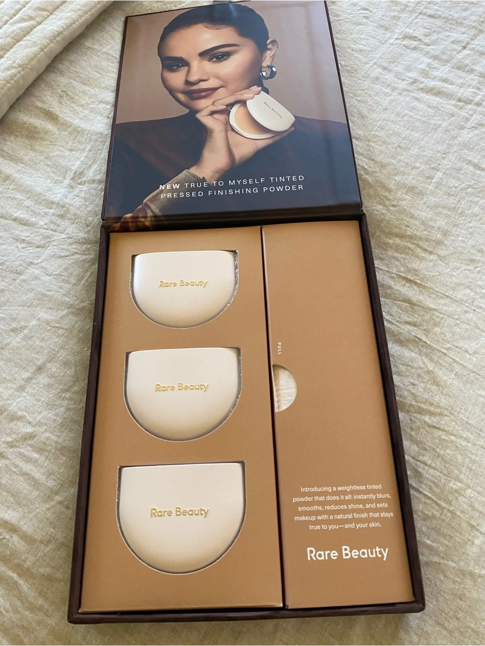 Rare Beauty pressed powder compacts in warm beige and tan tones